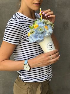 a woman holding a cup with flowers and a straw in it while looking at the camera