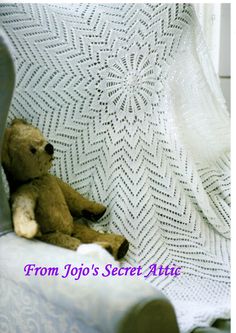 a brown teddy bear sitting on top of a white chair next to a crocheted blanket