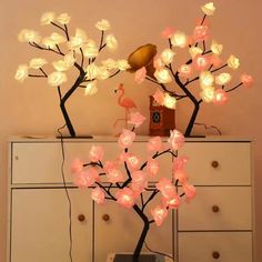 a lamp that is sitting on top of a dresser next to a tree with pink flowers