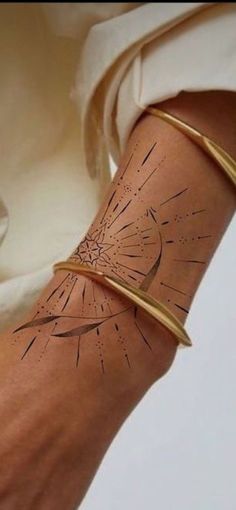 a woman's arm with a gold bracelet and starburst tattoo on it