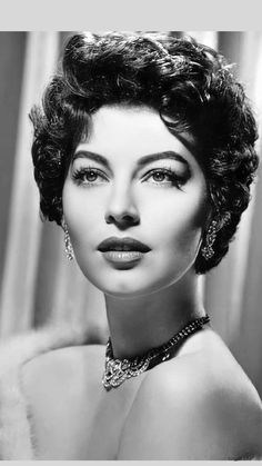 a black and white photo of a woman with short hair wearing an evening dress, necklace and earrings