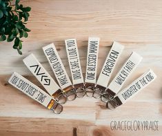 six white key chains with black letters on them sitting on a wooden table next to a potted plant