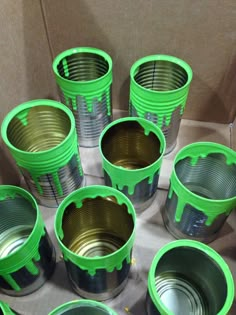 several green cups sitting on top of a cardboard box filled with tins and lids