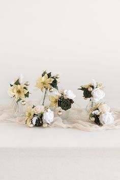 three vases filled with flowers sitting on top of a white cloth covered tablecloth