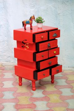 a red dresser with drawers and a toy horse on top