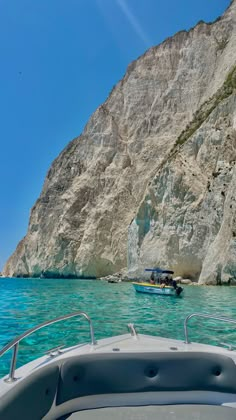 a boat is in the water next to a large rock face and another boat near it