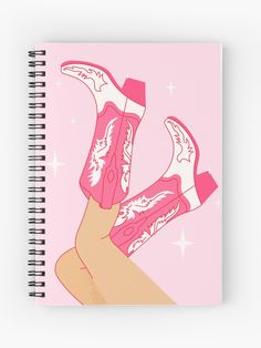 a spiral notebook with an illustration of pink cowboy boots and stars on the cover, in front of a pink background