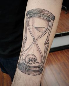 a man's arm with an hourglass tattoo on it and a skull in the sand