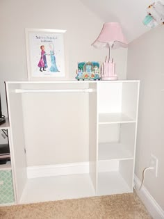 a white book shelf in the corner of a room with a pink lamp on top