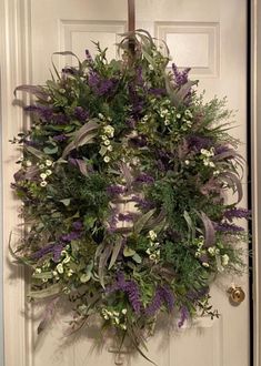 a wreath hanging on the front door of a house with purple flowers and greenery