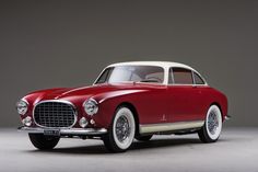 a red and white classic car parked in a room with gray walls, black flooring and grey background