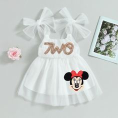 a white dress with minnie mouse sequins on it and a pink rose next to it