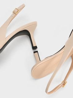 a pair of nude colored shoes with black and gold details on the heel, side view