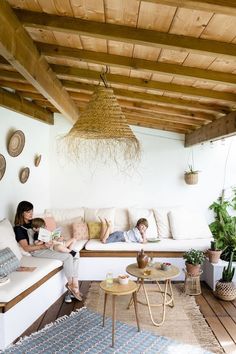 two people sitting on a couch in a room with wood beams and white walls, while one person is reading a book