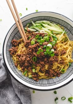 a bowl filled with noodles and meat on top of a white table next to chopsticks