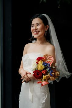 a woman in a white dress holding a bouquet of flowers and smiling at the camera