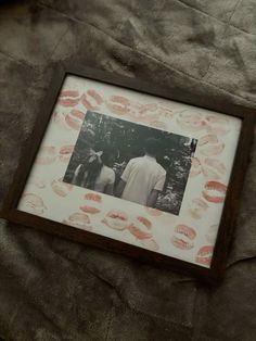 an old photo with red lipstick on it is laying on a bed sheet and there are two people standing in the background