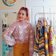 a woman is standing in front of some crocheted sweaters