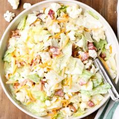 a salad with lettuce, bacon and cheese in a white bowl on a wooden table