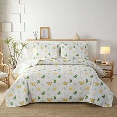 a white bed with yellow and green leaves on it in a room next to a chair