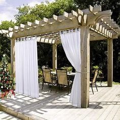 a wooden deck with white drapes on it and a christmas tree in the background