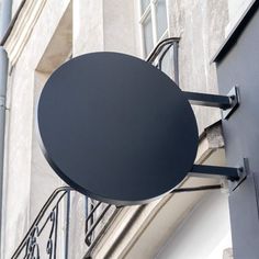 a black round sign hanging from the side of a building next to a metal hand rail