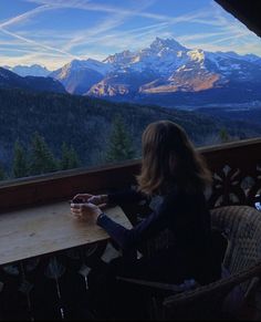 a woman sitting at a table looking out over the mountains and valleys in the distance