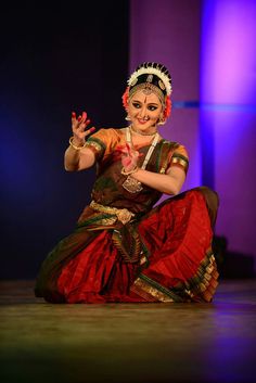 a woman in a red and green dress is dancing on the stage with her hands up