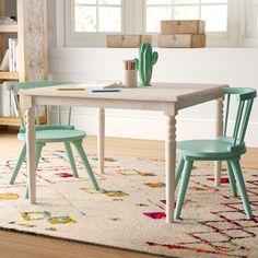 a white table with two green chairs and a rug on the floor in front of it