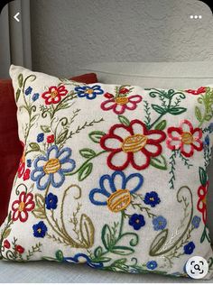 a white pillow with colorful flowers on it sitting on a red chair next to a gray wall