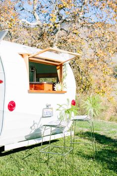 an old camper is parked in the grass with two chairs and a table on it