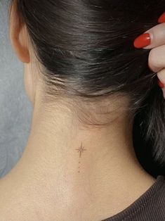 the back of a woman's neck with a small cross tattoo on her left side