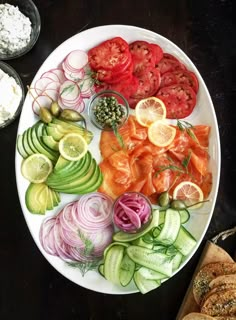 an assortment of vegetables on a white plate with bread and dips next to it