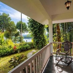 a rocking chair is on the front porch looking out at the lake and trees in the distance