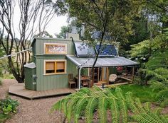 a small green house in the woods with lots of trees and plants around it, surrounded by greenery