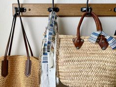 three woven bags hanging from hooks on a white wall next to two wooden pegs