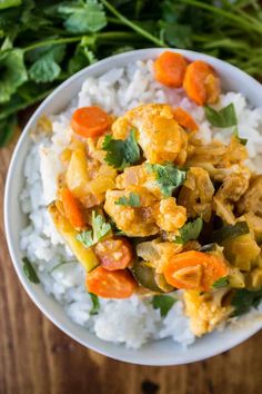 a white bowl filled with chicken and vegetables on top of rice next to carrots