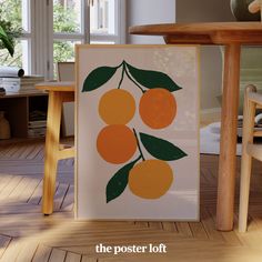 an orange print is on display in front of a wooden table with chairs and a potted plant