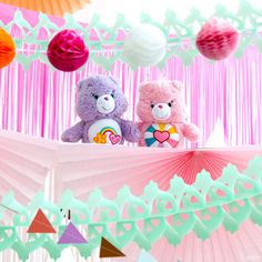 two teddy bears sitting on top of a pink and green table cloth with paper decorations