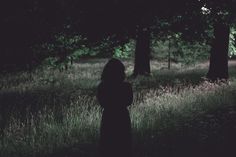 a woman standing in the middle of a forest with her back turned to the camera