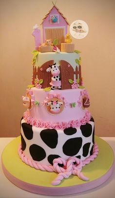 a three tiered cake decorated with pink and black polka dots, farm animals, and houses