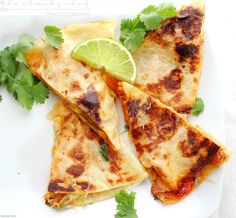 four quesadillas on a white plate with lime wedges and cilantro