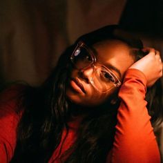 a woman wearing glasses sitting in the dark with her hand on her head and looking off to the side