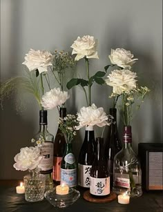 several bottles and vases with flowers in them sitting on a table next to candles