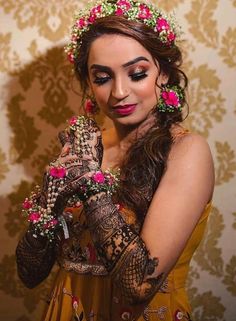 a woman with flowers in her hair is wearing henna and holding hands up to her face