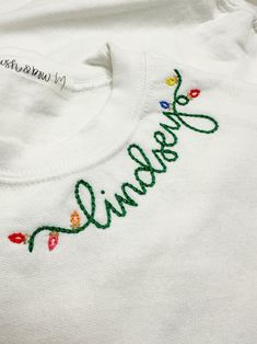 a white t - shirt with embroidered name and flowers on the front, sitting on a table