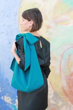 a woman standing in front of a wall wearing a black dress with a green bow on it