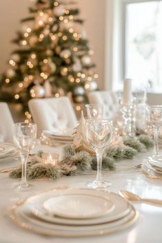 a table set for christmas dinner with white plates and silverware in front of a decorated christmas tree