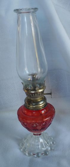 a red glass vase sitting on top of a white cloth covered table next to a light bulb