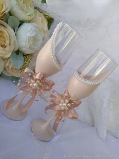 two champagne flutes with bows and pearls on them, sitting next to some white flowers